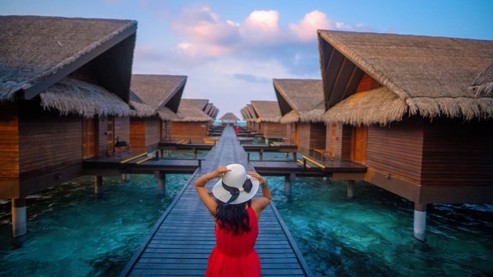 Woman looking at a pool in front of hotel or condos. She is wearing a red dress and white hat.